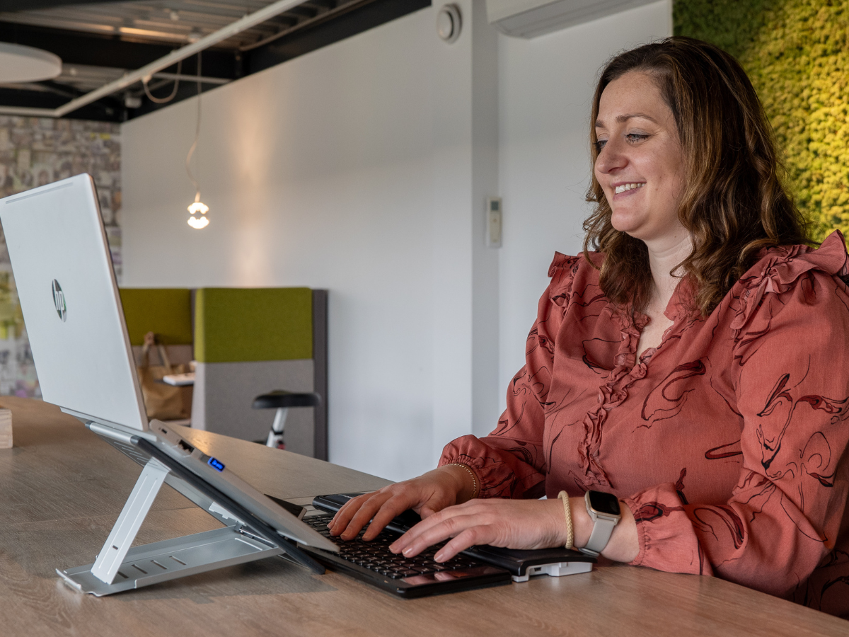 Vrouw achter een laptop met ergonomisch toetsenbord.