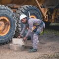 Werknemer met helm en het Hapo exoskelet, bezig met het tillen van zware blokken op een industriële werklocatie